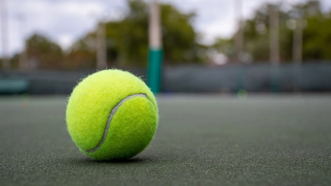 A close-up of a fuzzy tennis ball resting on a court, highlighting the texture that enhances grip and control during play. Why Are Tennis Balls Fuzzy ?